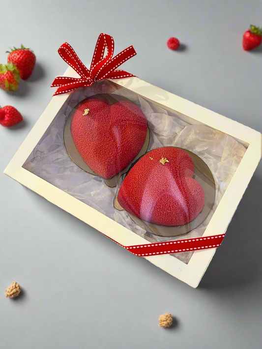 two mini heart shaped mousse dessert in white box on the grey background with some strawberries