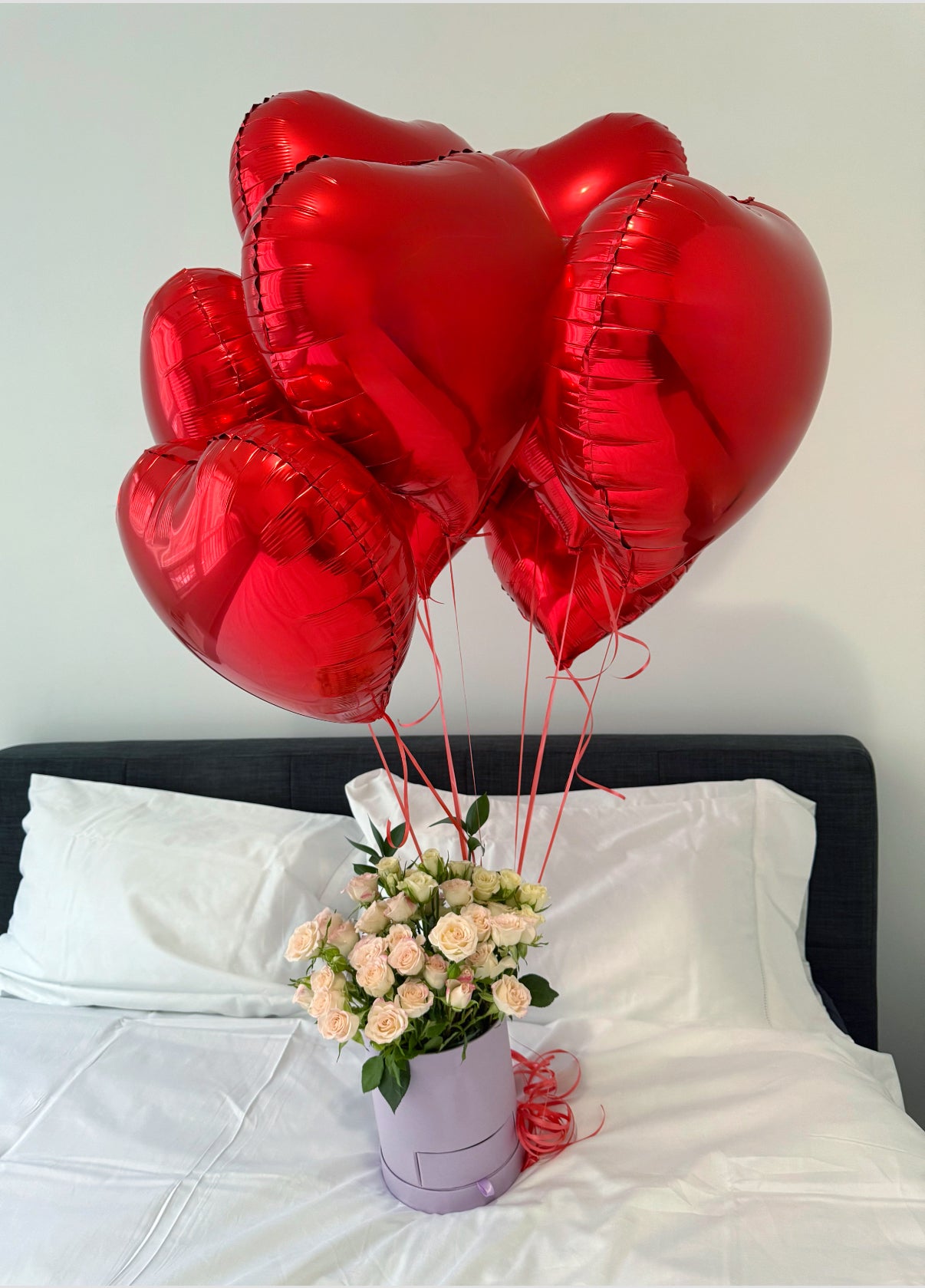 Heart balloons with box of roses on the bed