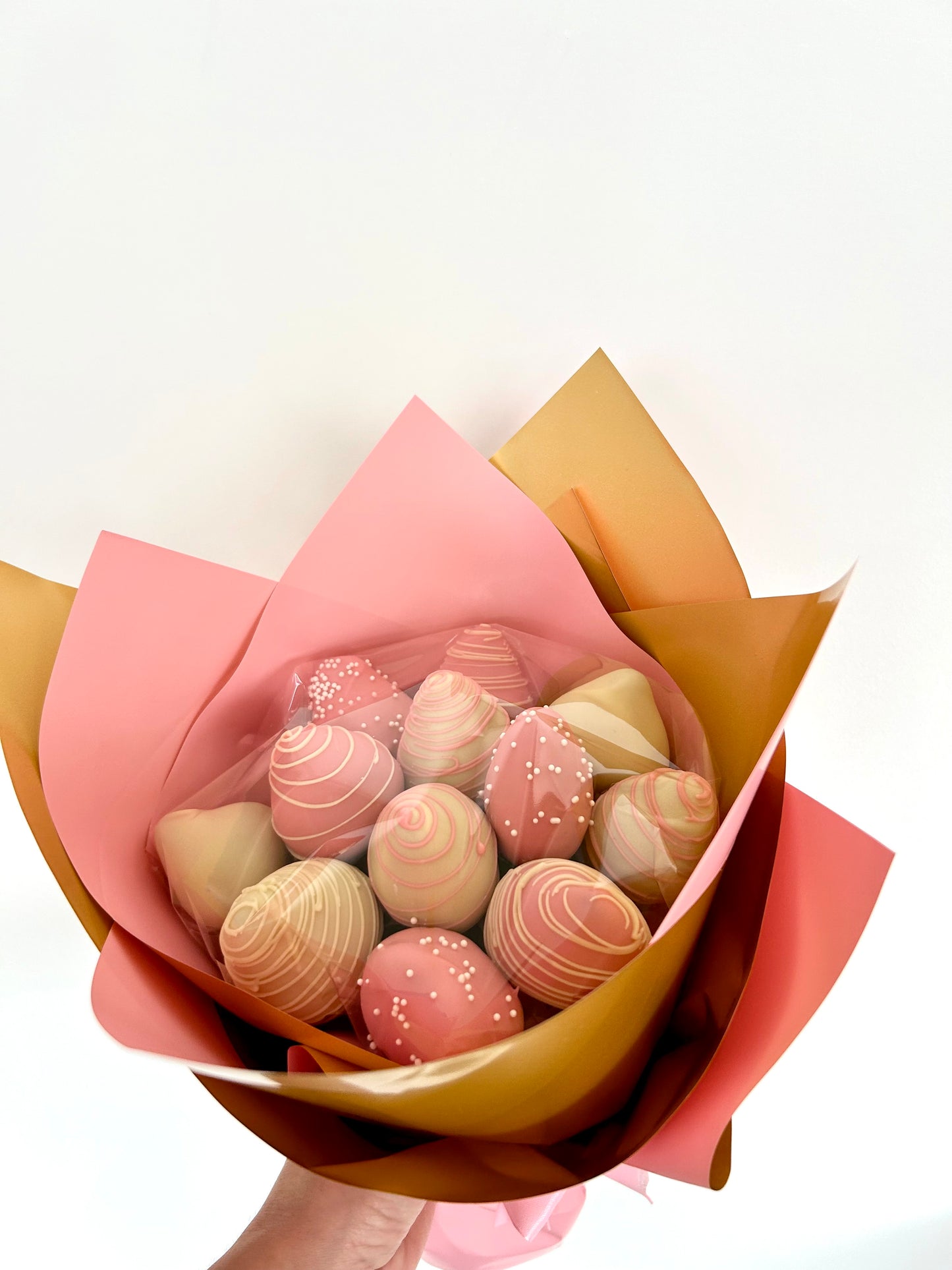 hand holds bouquet of chocolate covered strawberries in pink and gold wrapping 