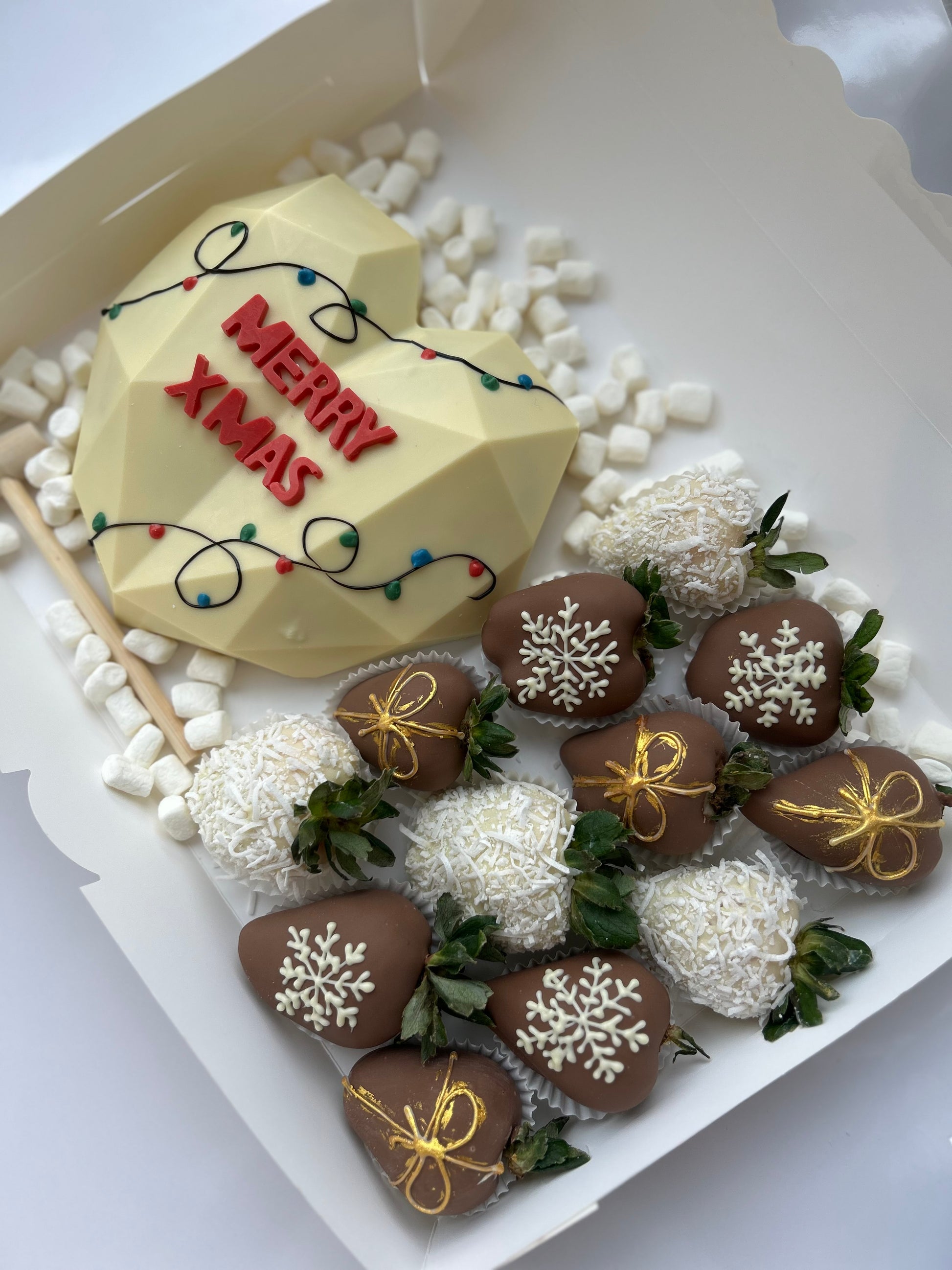 Heart-shaped cake with 'Merry Xmas' text and decorated strawberries on a white background
